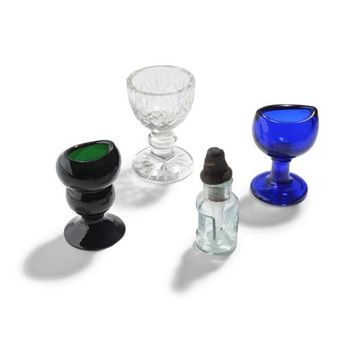 77 · THREE GLASS EYE BATHS AND AN EYE DROP BOTTLE